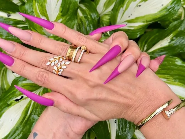 Neue lila Farbe Lange Nägel, scharfe Stilettos, Handflächen, lange Finger im Garten mit Blumen